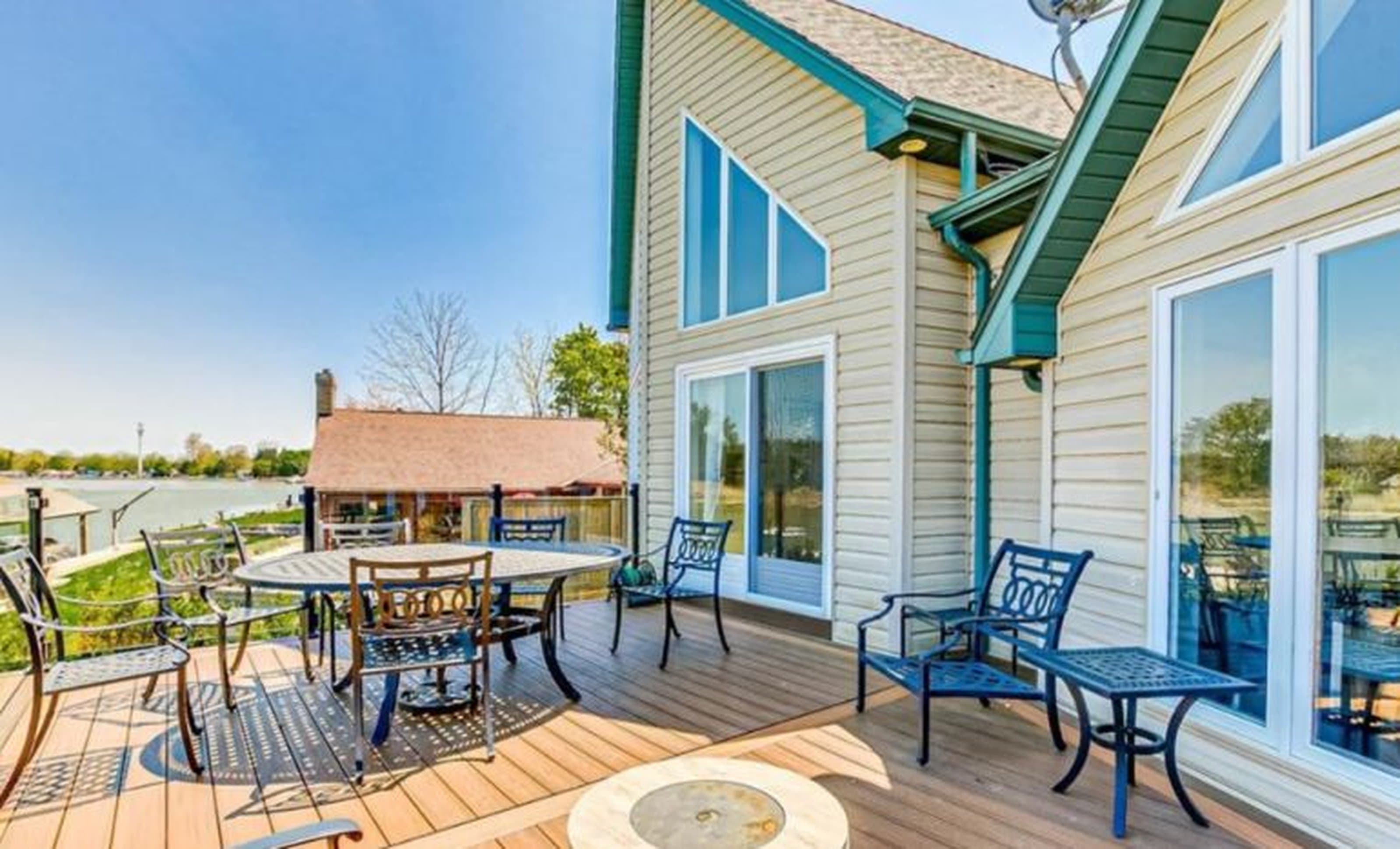 Wooden deck with blue metal patio furniture overlooking a scenic lake on a sunny day.